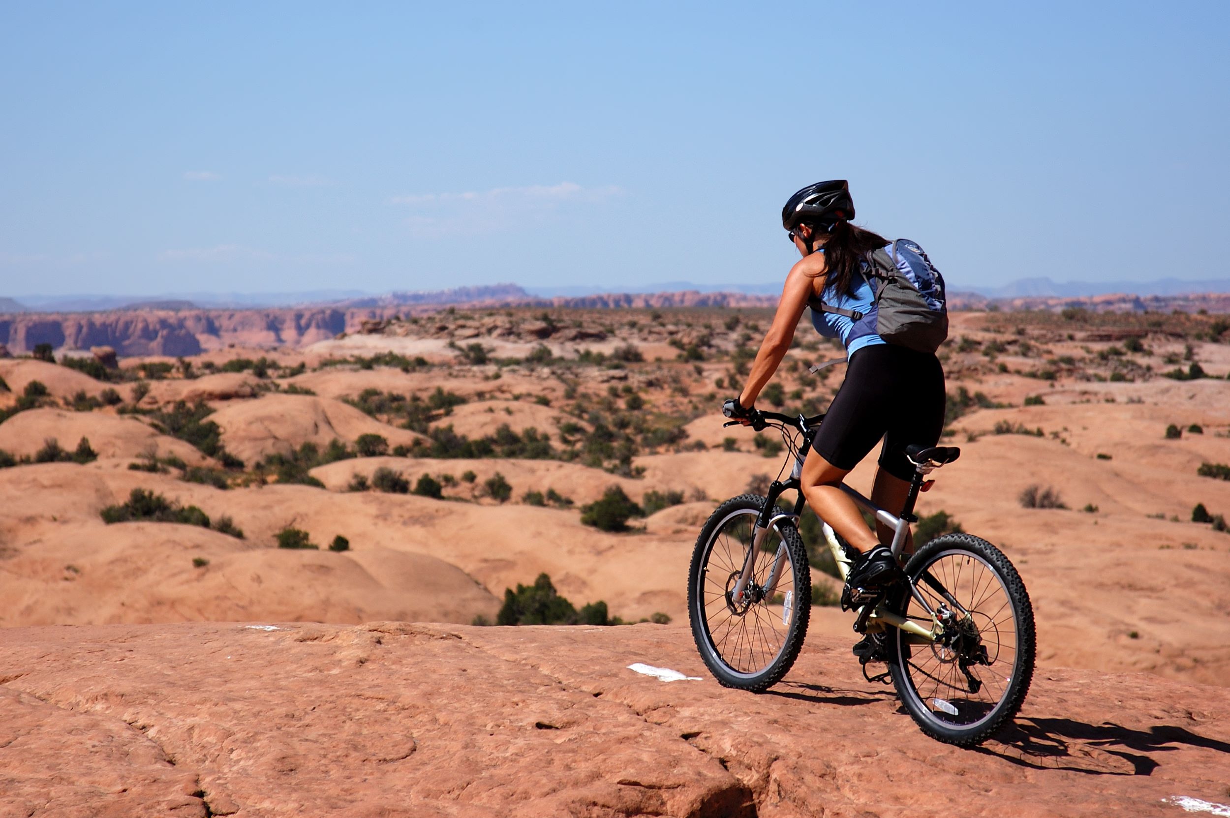 A woman riding her bike across a red rock trail.