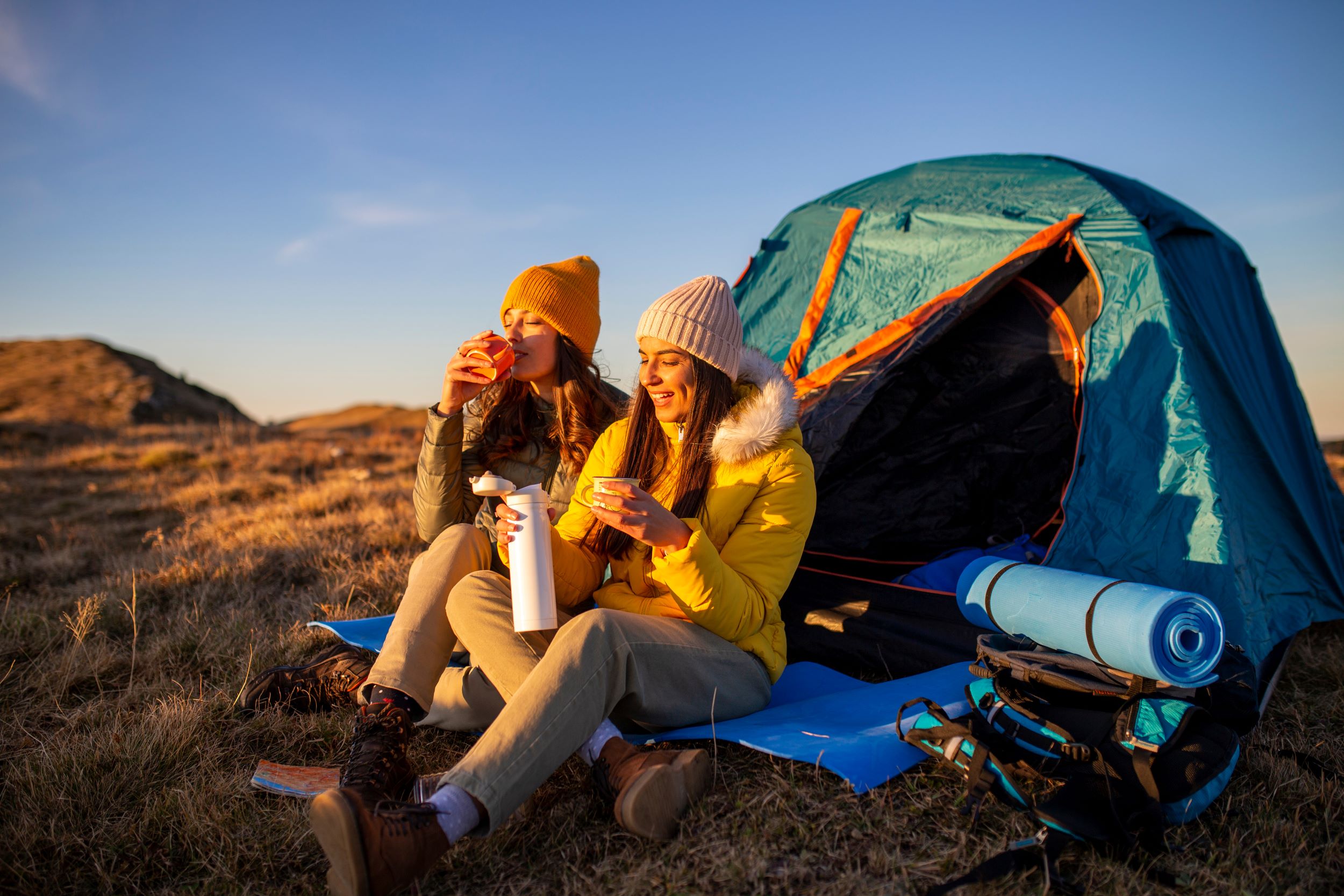 Two women drinking coffee at sunrise in front of their tent.
