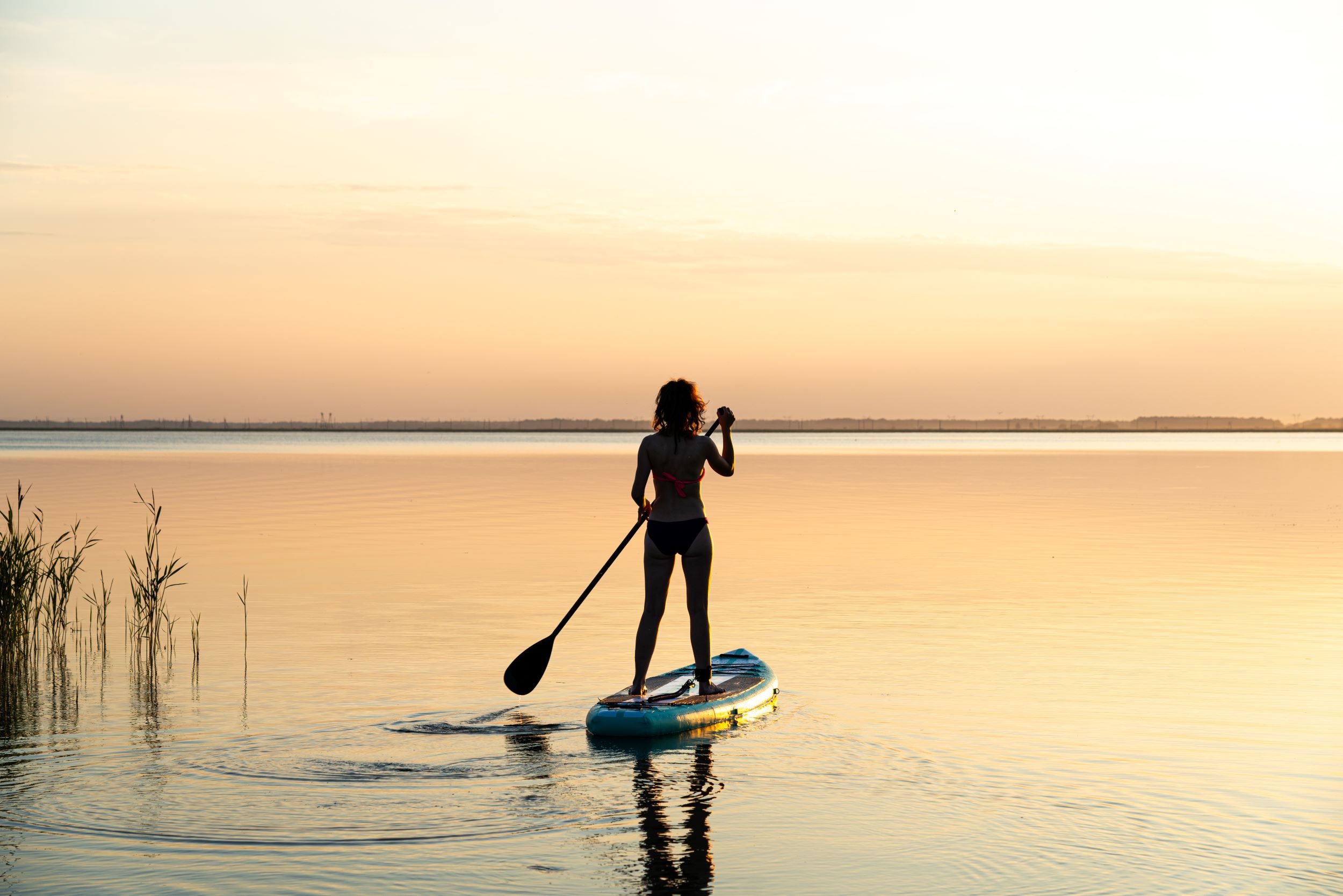 A woman paddle boarding at sunset.